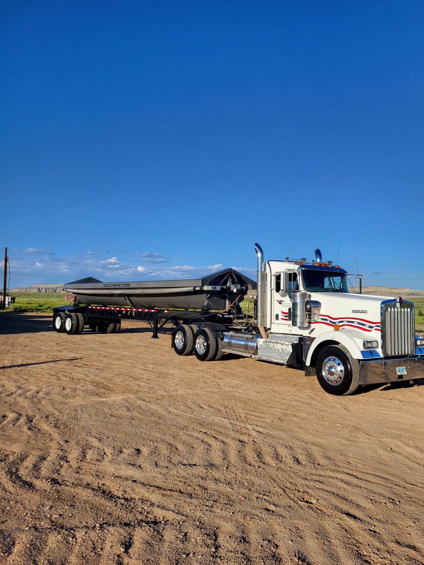 Buck's Trucks white Kenworth hauling an oversize boat on a step deck
